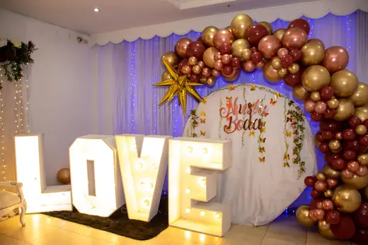 Letras luminosas LOVE bajo un arco de globos dorados
