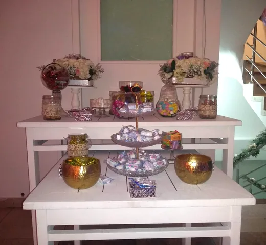 Mesa de dulces montada en el salón, con bomboneras de vidrio, marshmallows y arreglos florales blancos