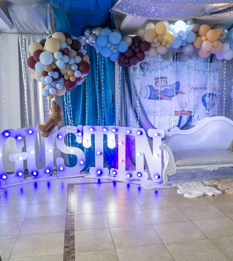 Letras luminosas con el nombre del niño, arco de globos en tonos pastel y sofá blanco para las fotos