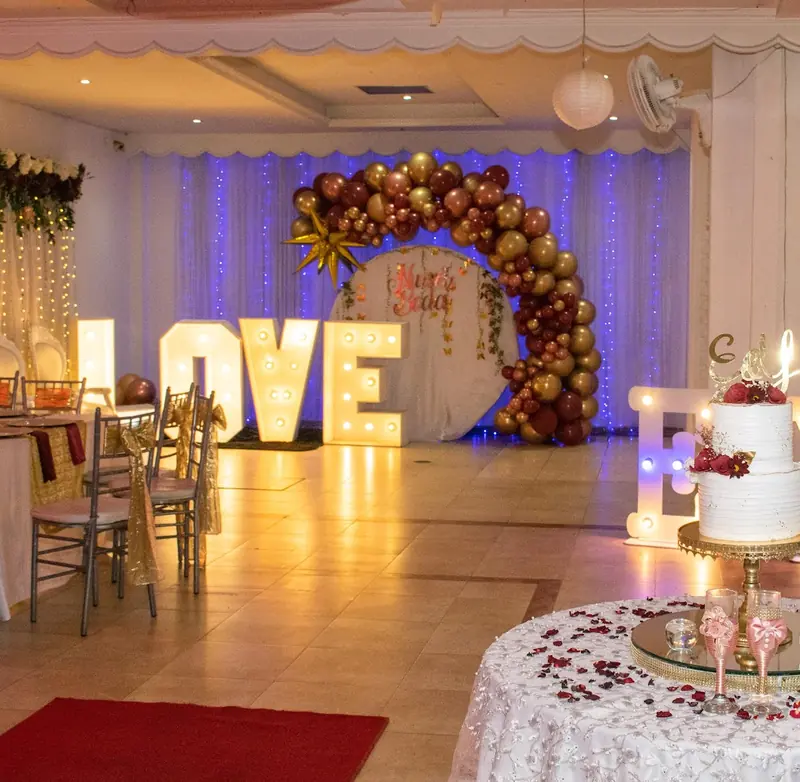 Letras luminosas LOVE, arco de globos vino y dorado, alfombra roja y mesa de torta de boda