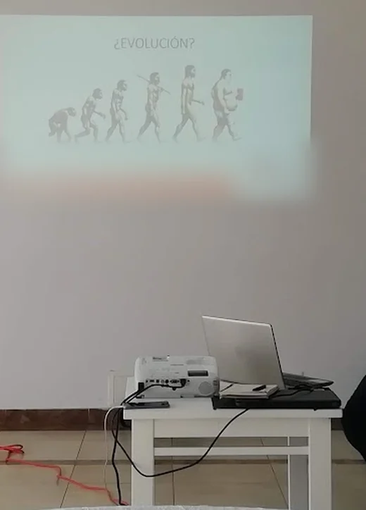 Videobeam y portátil sobre una mesa del salón, con la presentación proyectada en la pared